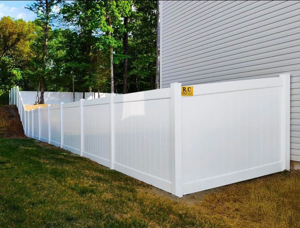 White vinyl privacy fence bordering a yard, next to a white house and treeline.