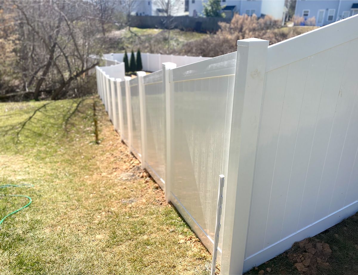 White vinyl fence along a grassy yard, with trees and houses visible in the background.