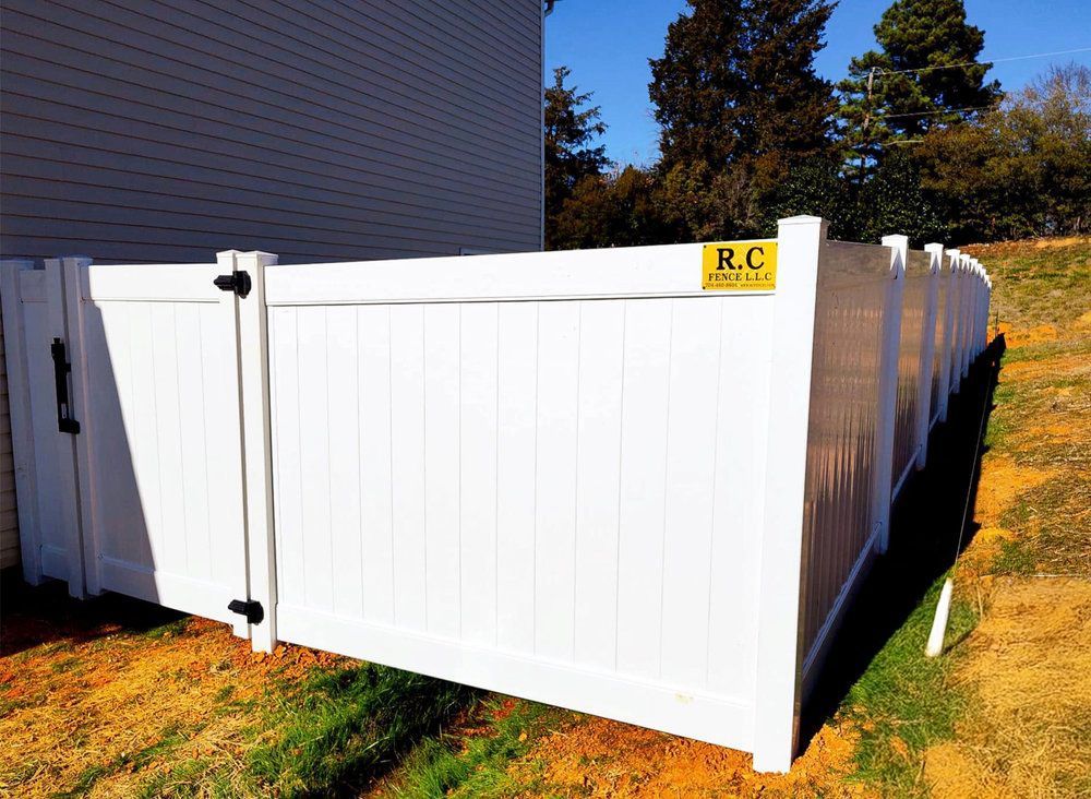 White vinyl fence and gate installed in a yard, bordering a building. A yellow sign on the fence reads