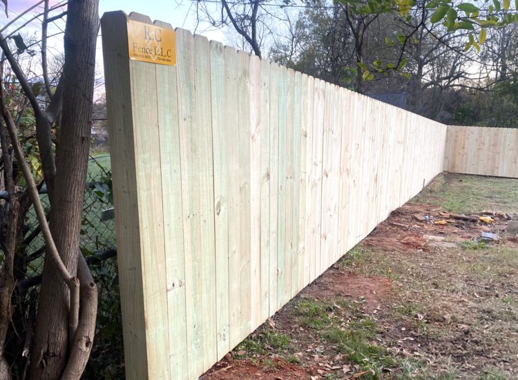 Wooden fence running along a grassy yard, trees in the background.