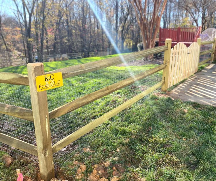Wooden split-rail fence with attached chicken wire, featuring a small gate section. A company sign is attached to a post.