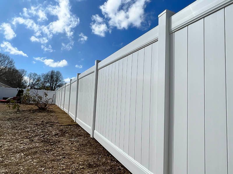White vinyl fence against a blue sky with scattered clouds, running along a brown yard.