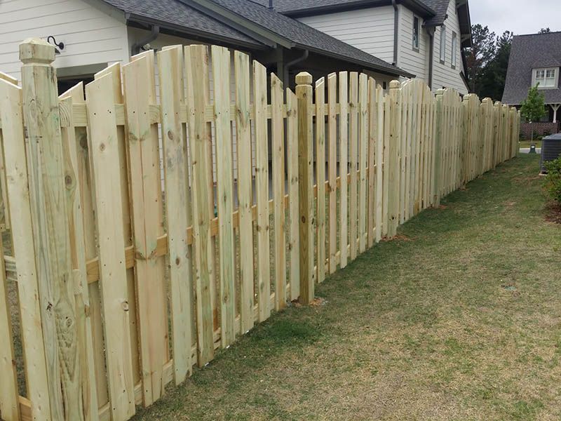 Wooden picket fence surrounding a grassy yard, with a house in the background.