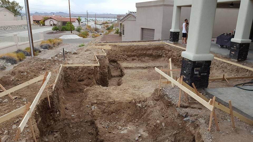 A large hole in the ground in front of a house under construction.