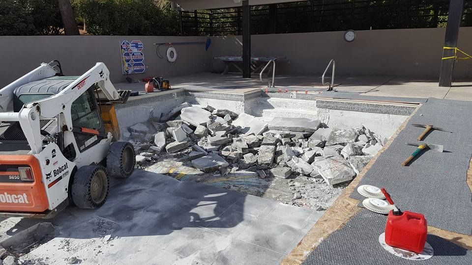 A bobcat is being used to remove concrete from a pool.