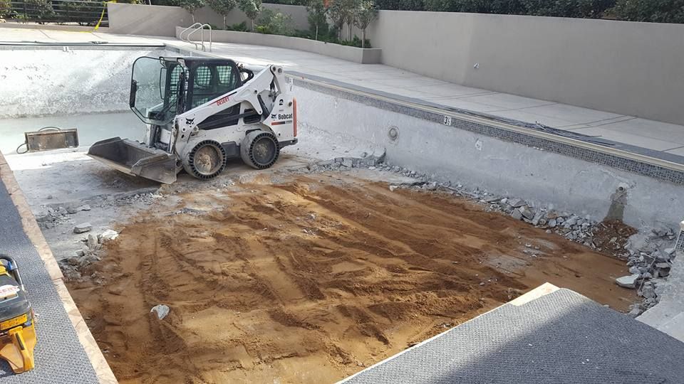 A bulldozer is moving dirt around a swimming pool.