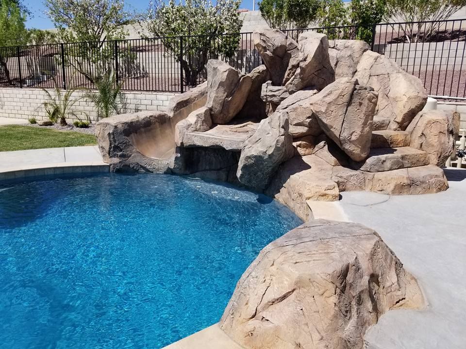 A swimming pool with a water slide and rocks surrounding it