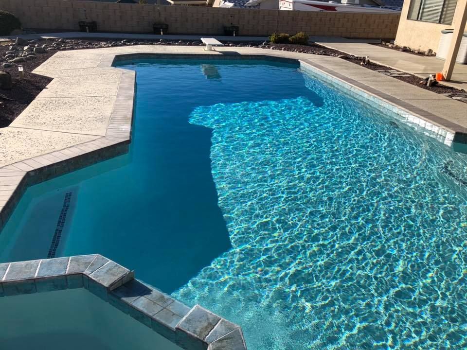 A large swimming pool with a concrete deck and stairs leading to it.