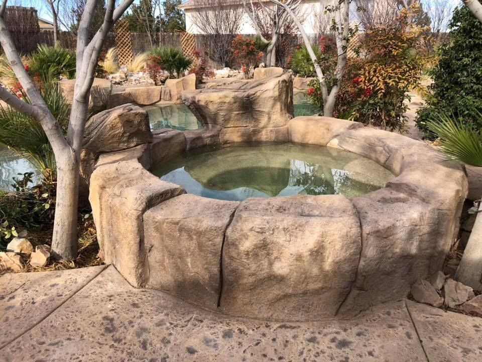 A hot tub surrounded by rocks and trees in a garden