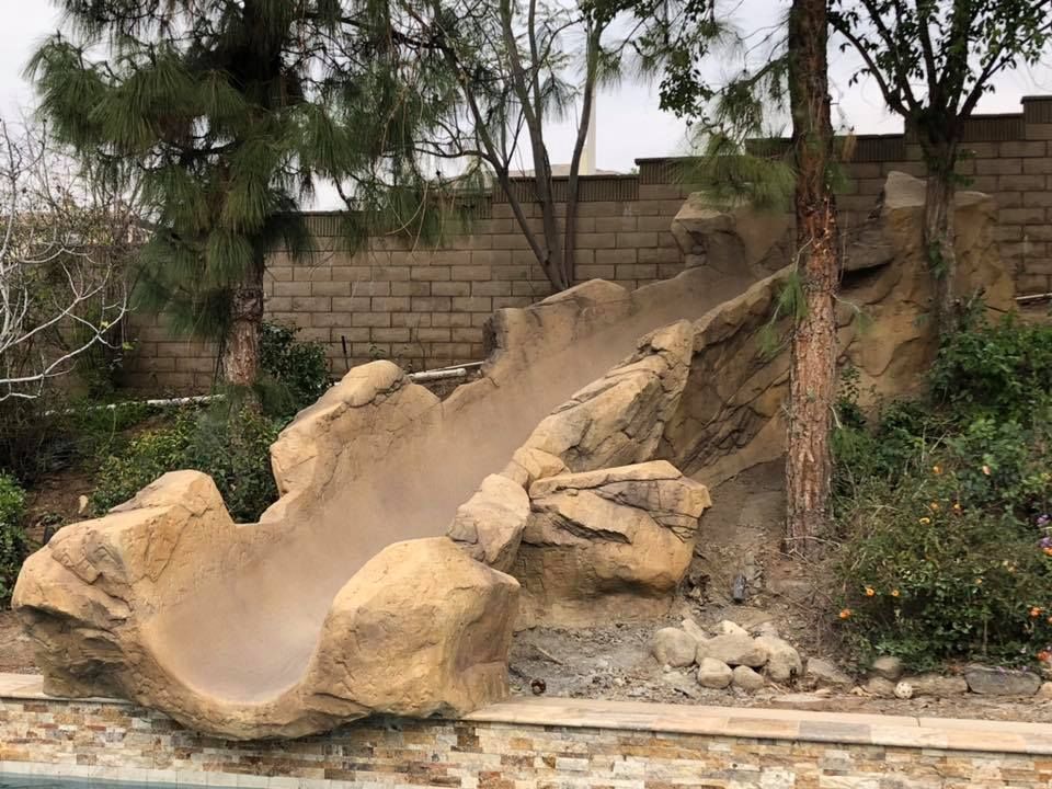 A large rock slide is sitting next to a swimming pool.