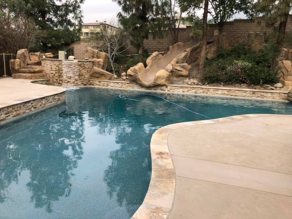 A large swimming pool surrounded by trees and rocks in a backyard.