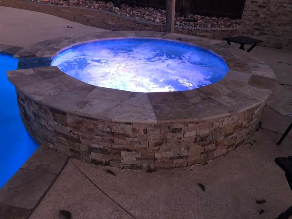 A hot tub is lit up at night next to a pool.