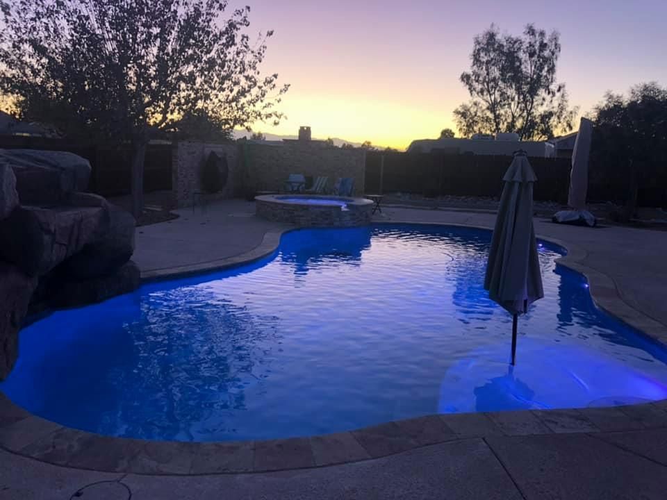 A large swimming pool is lit up at night with a sunset in the background.