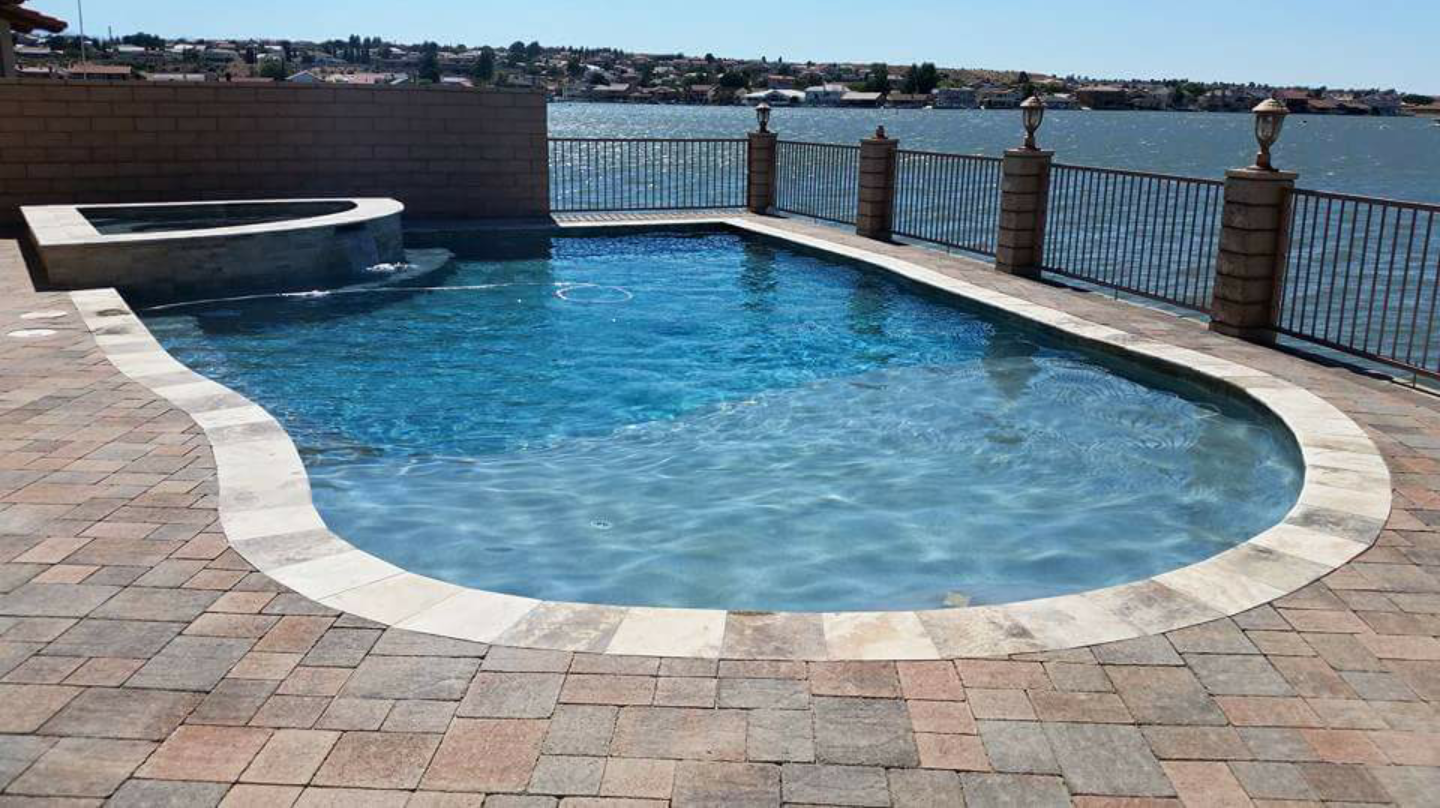 A large swimming pool surrounded by bricks next to a body of water.