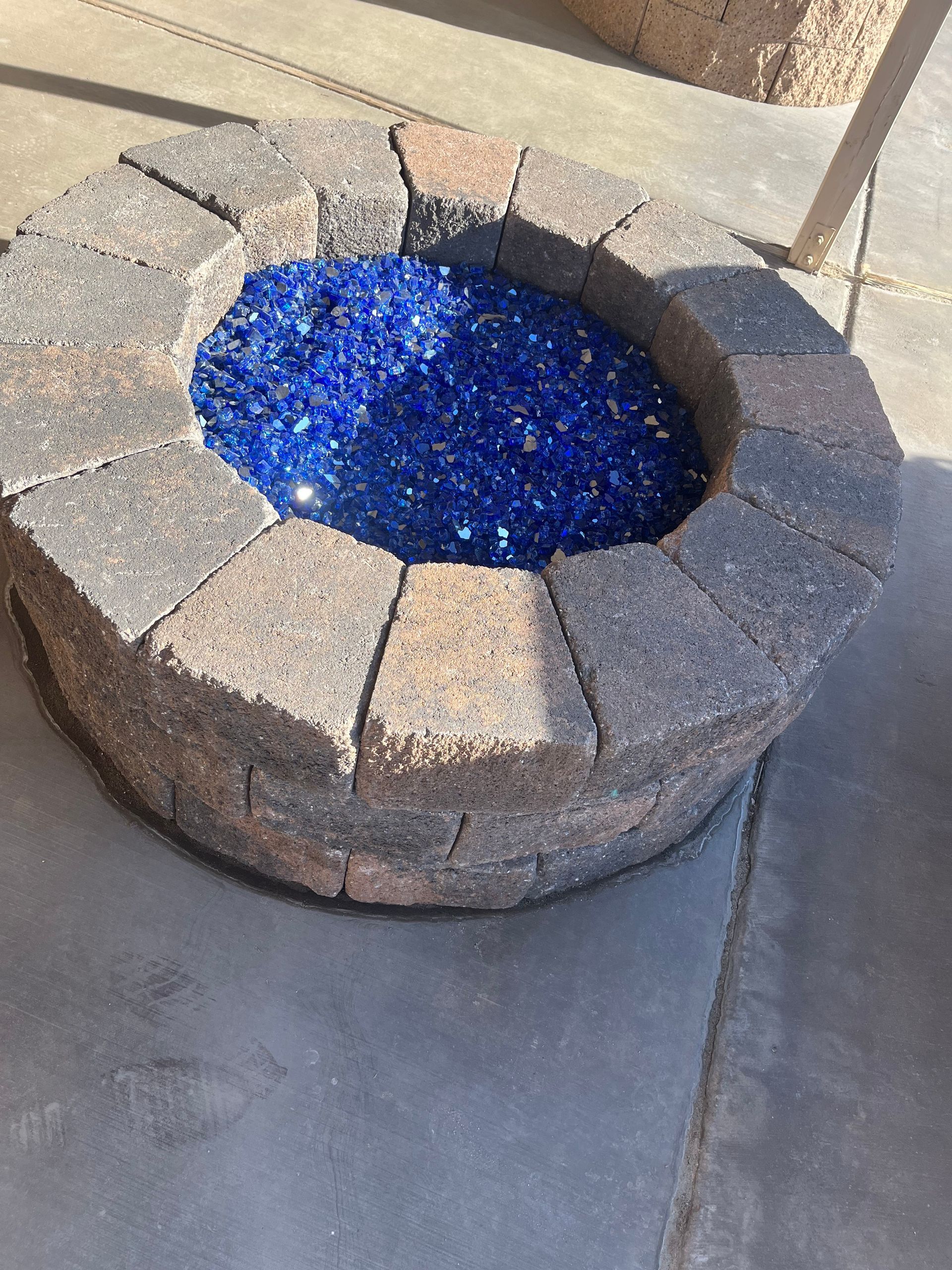 A fire pit filled with blue glass beads on a concrete surface.