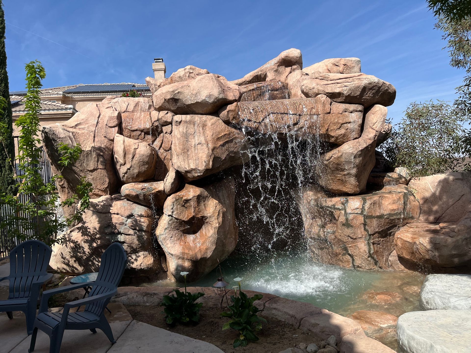 A waterfall is surrounded by large rocks in a backyard.