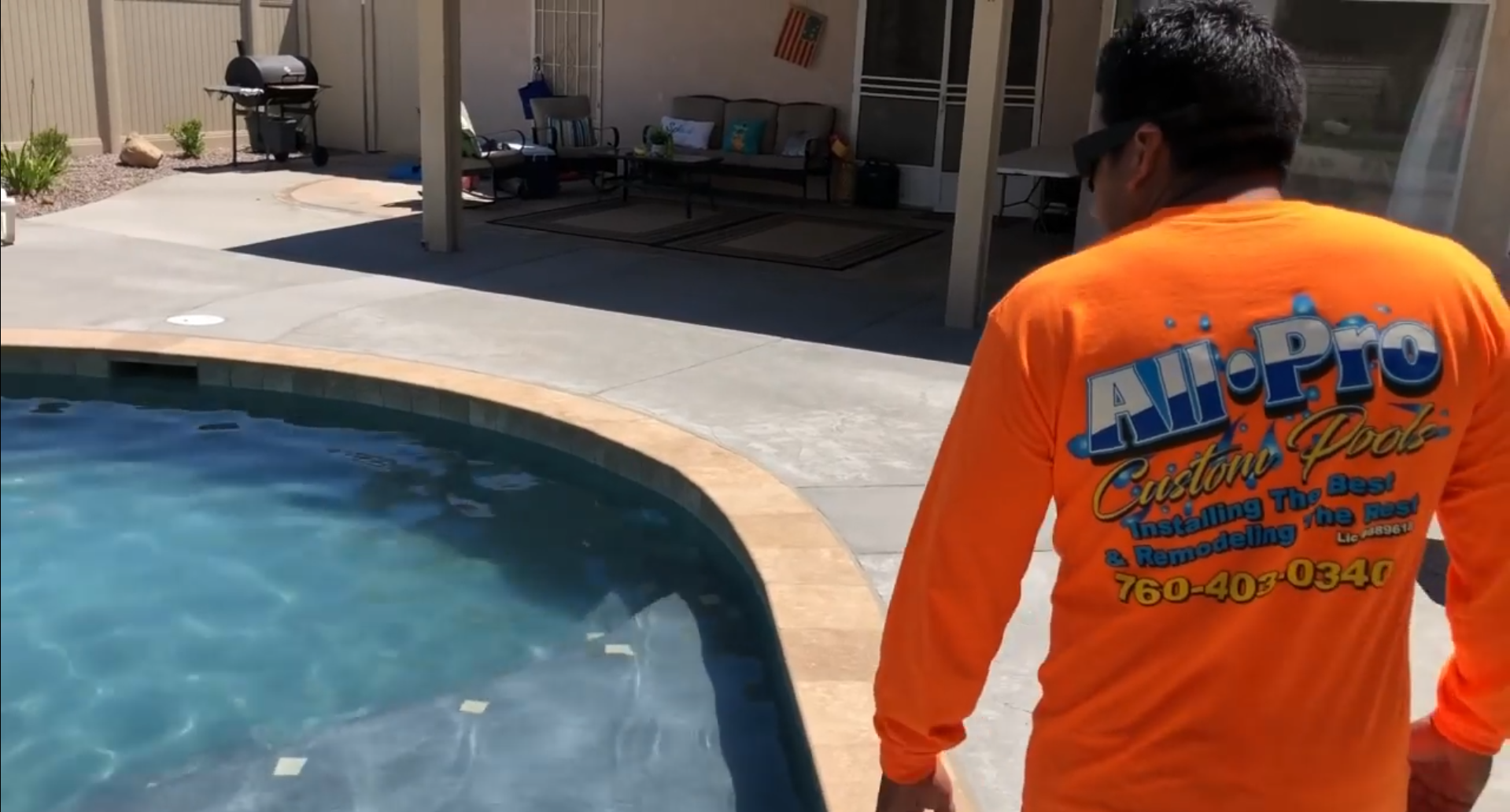 A man in an orange shirt is standing next to a pool.