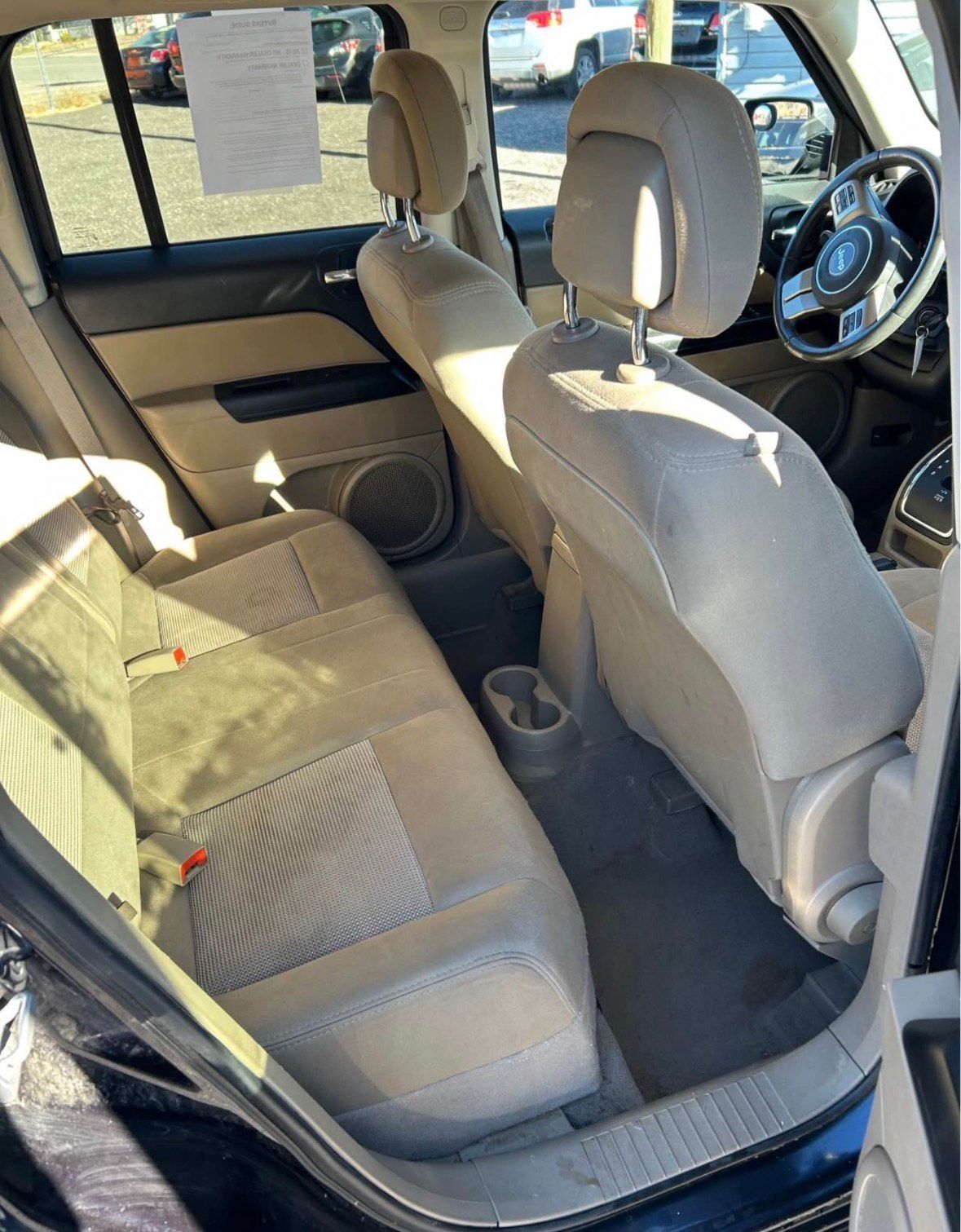 Backseat of a tan-interior vehicle, showing seats, floor, and a glimpse of the steering wheel.