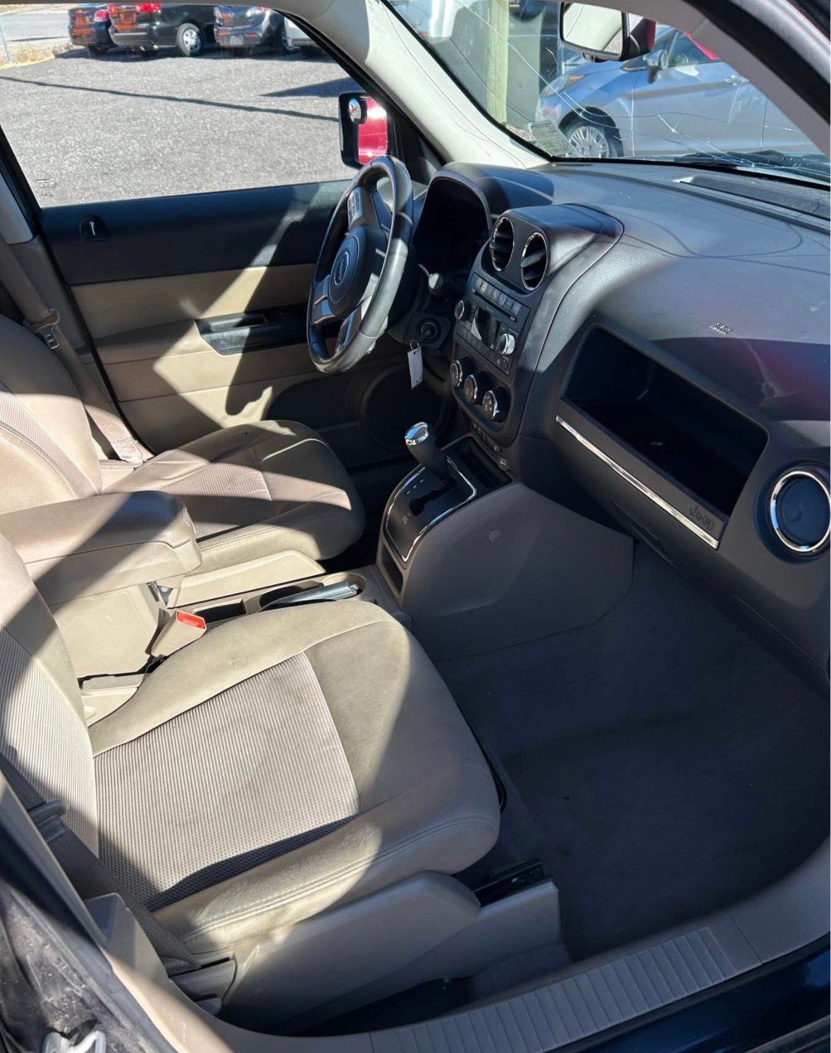 Interior of a vehicle, tan seats, black dashboard and steering wheel, visible driver's side.
