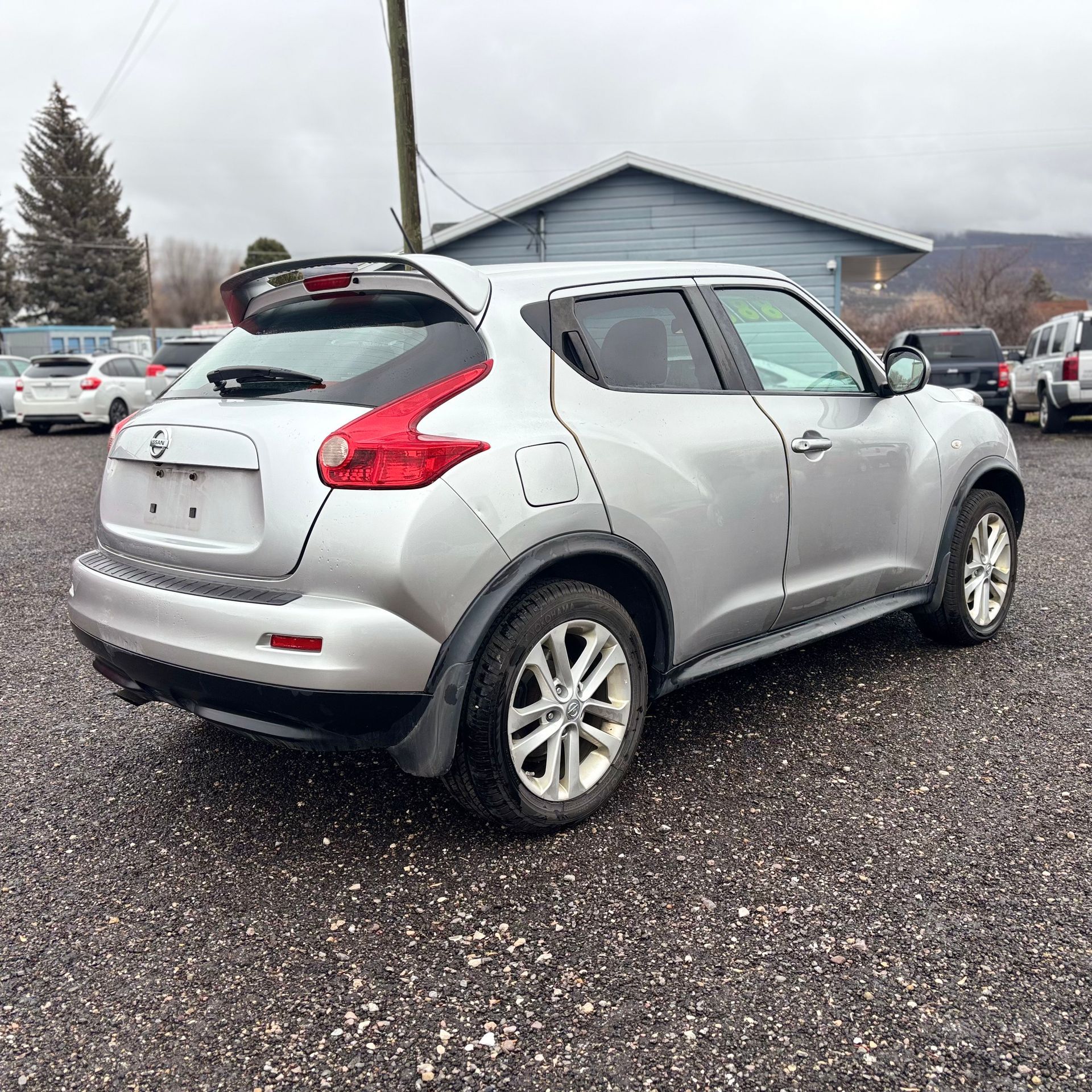 Silver Nissan Juke SUV parked on gravel, cloudy sky in background.
