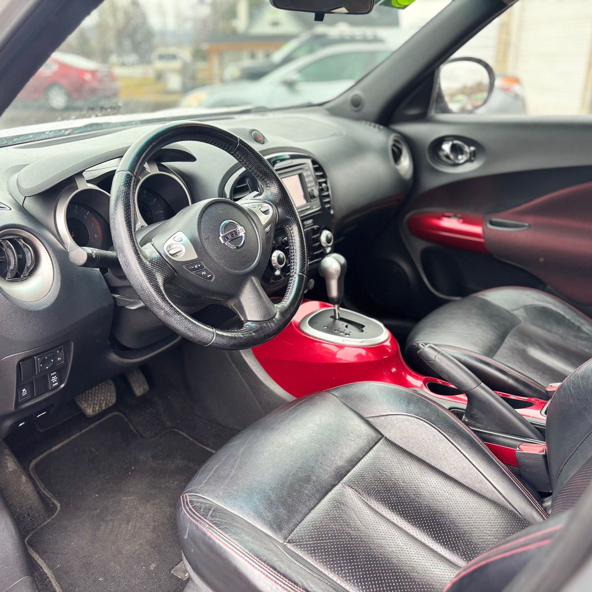 Interior of a Nissan Juke, black leather seats, red console, black steering wheel.