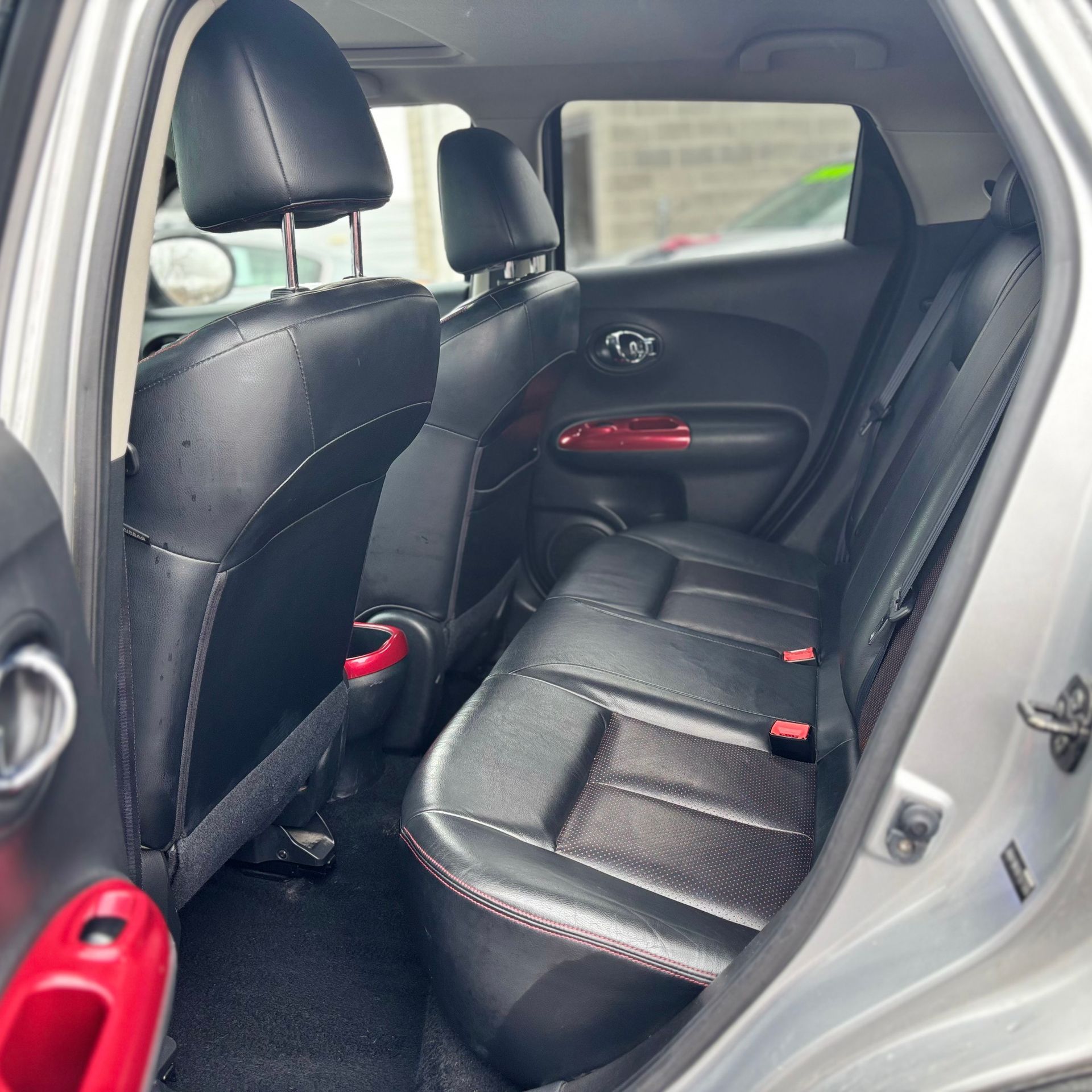 Interior view of a silver Nissan Juke, showing black leather back seats with red stitching and accents.