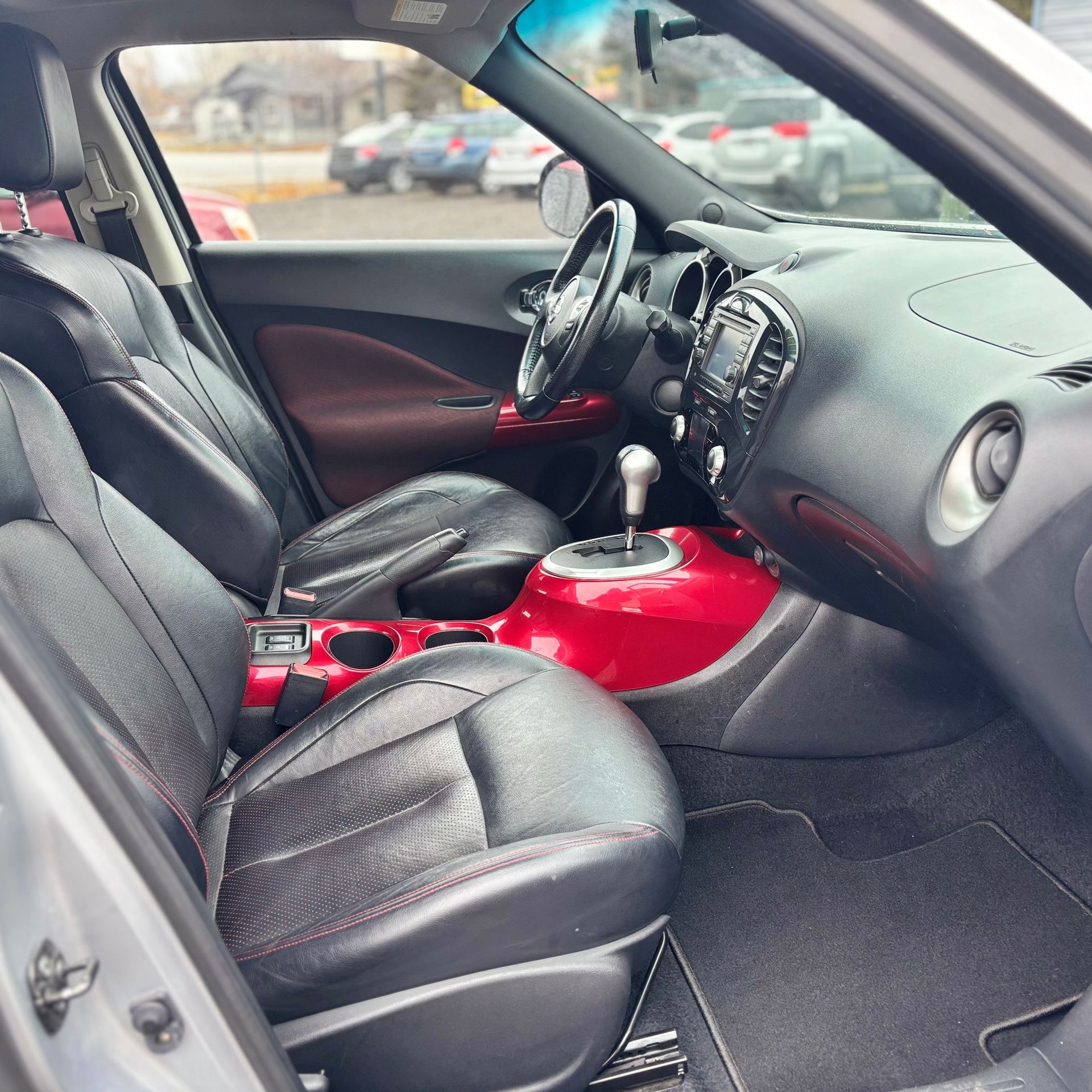 Interior of a car; black leather seats, red console, silver trim.