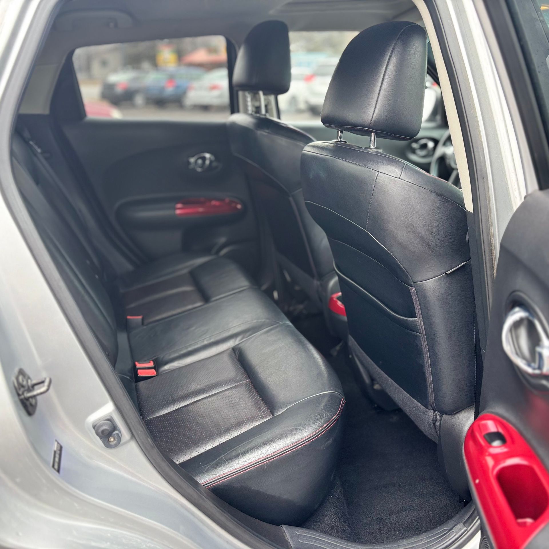 Interior view of a silver Nissan Juke, showing black leather back seats with red stitching and accents.