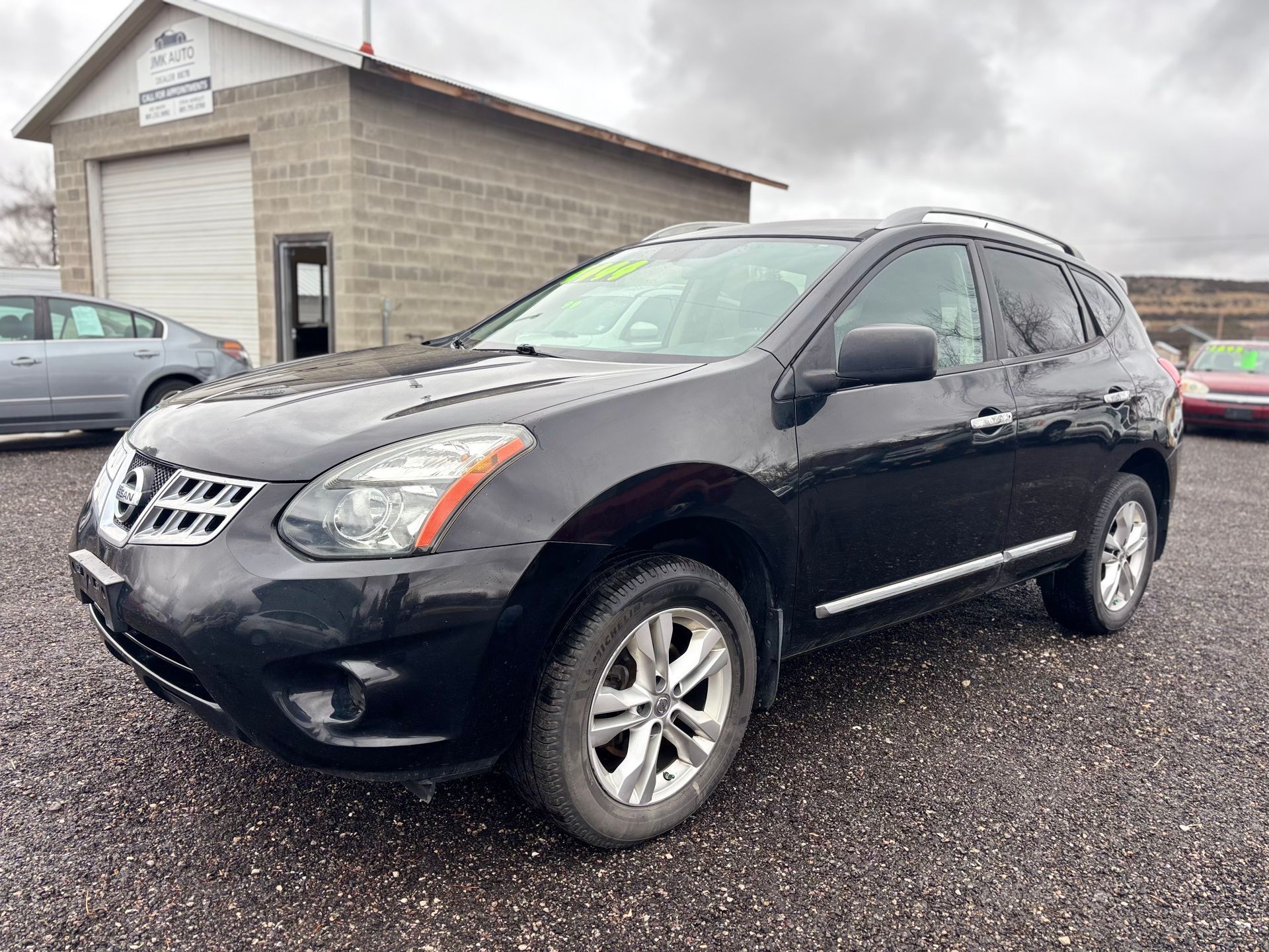 Black Nissan Rogue SUV parked in front of a gray garage on a cloudy day.