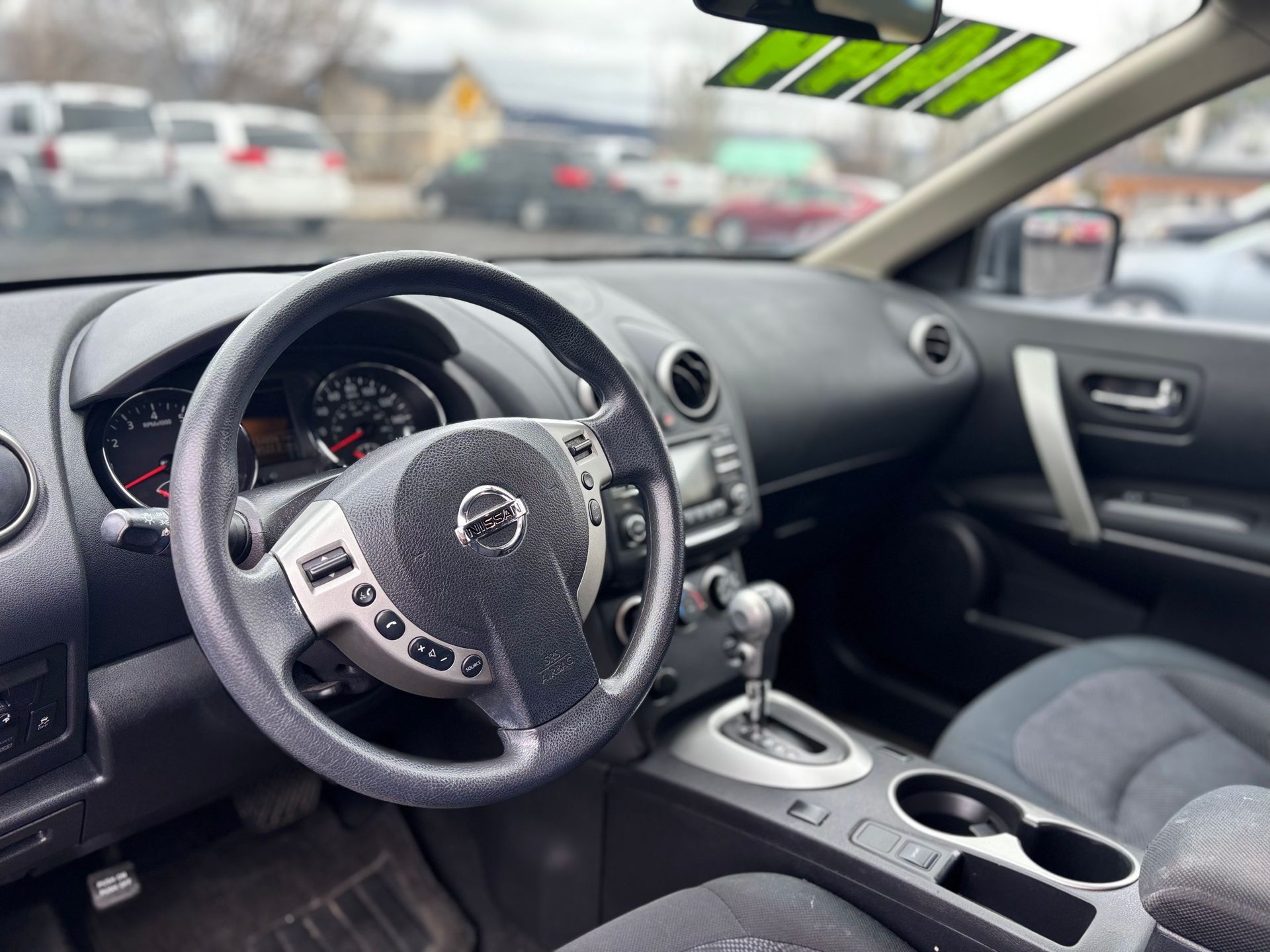 Interior of a Nissan Rogue, showing the steering wheel, dashboard, gear shift, and cup holders.
