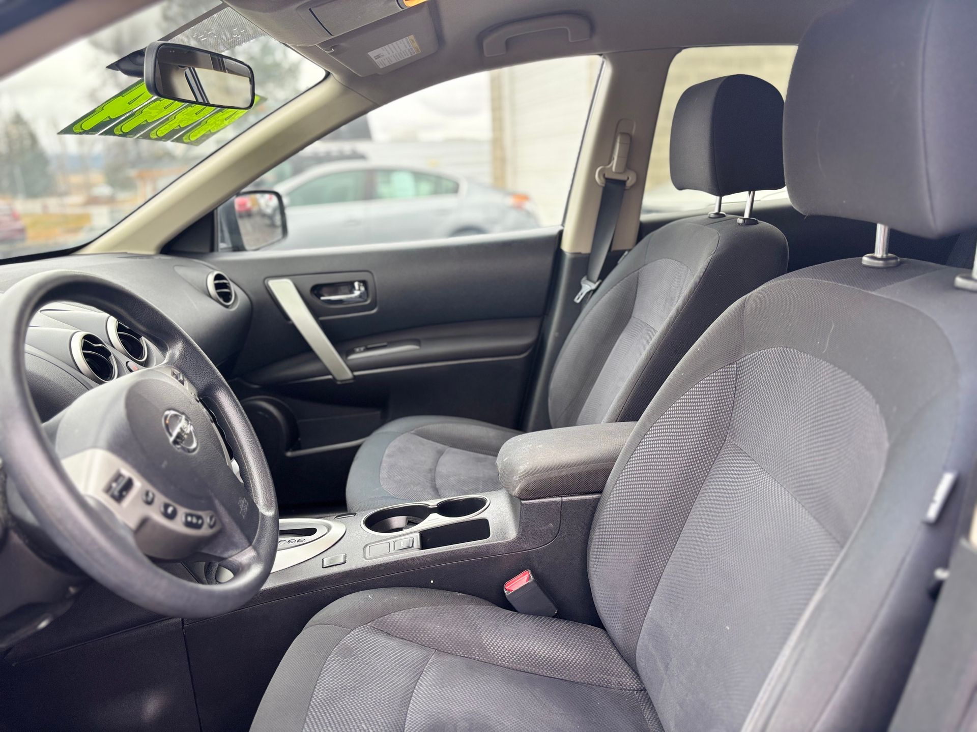 Interior of a Nissan Rogue, showing driver's seat, dashboard, and center console with cup holders. Gray seats.