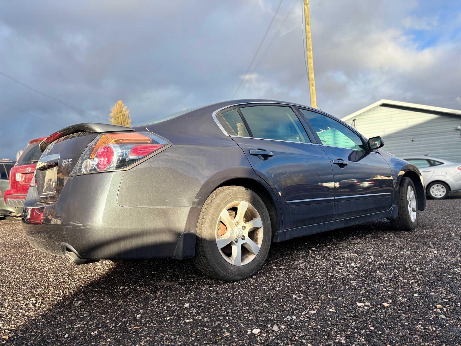 Dark gray sedan parked on gravel in a sunny outdoor setting.