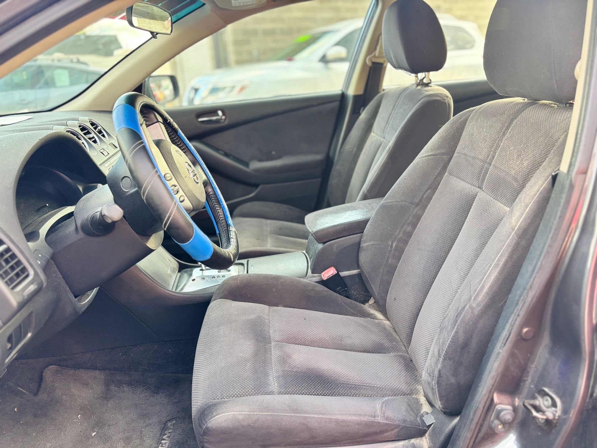 Interior view of a car with black cloth seats and a blue steering wheel cover.