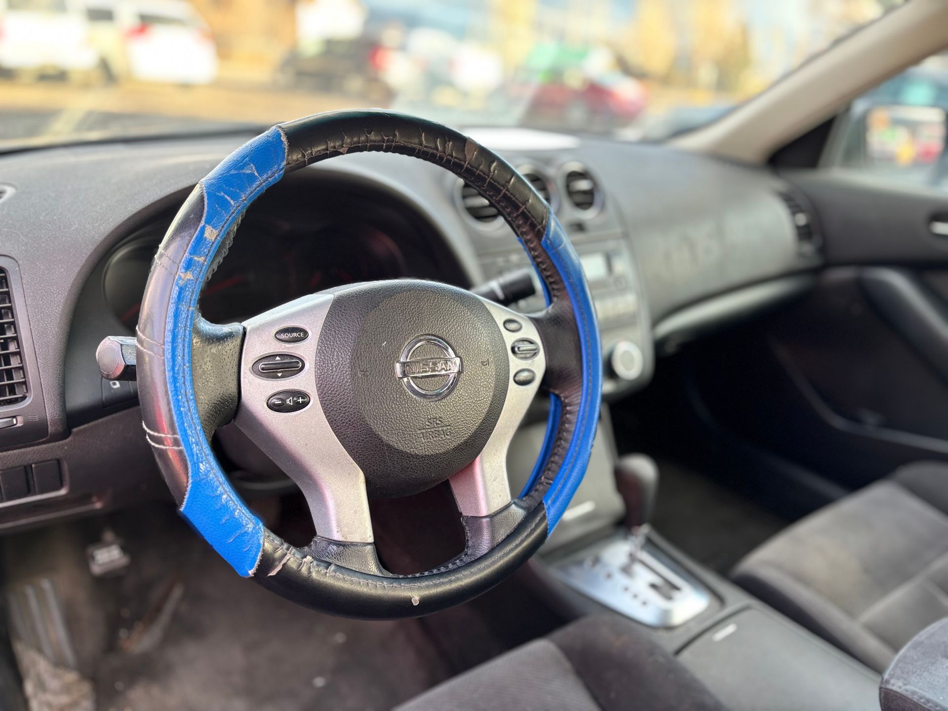 Interior view of a car with a steering wheel covered with a blue and black steering wheel cover.