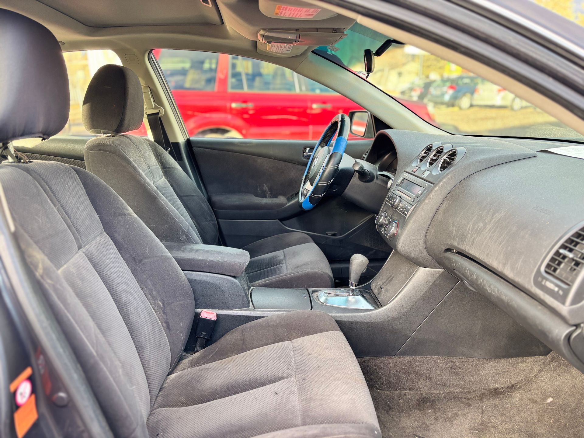 Car interior with gray fabric seats, black dashboard, and steering wheel, looking to the side.