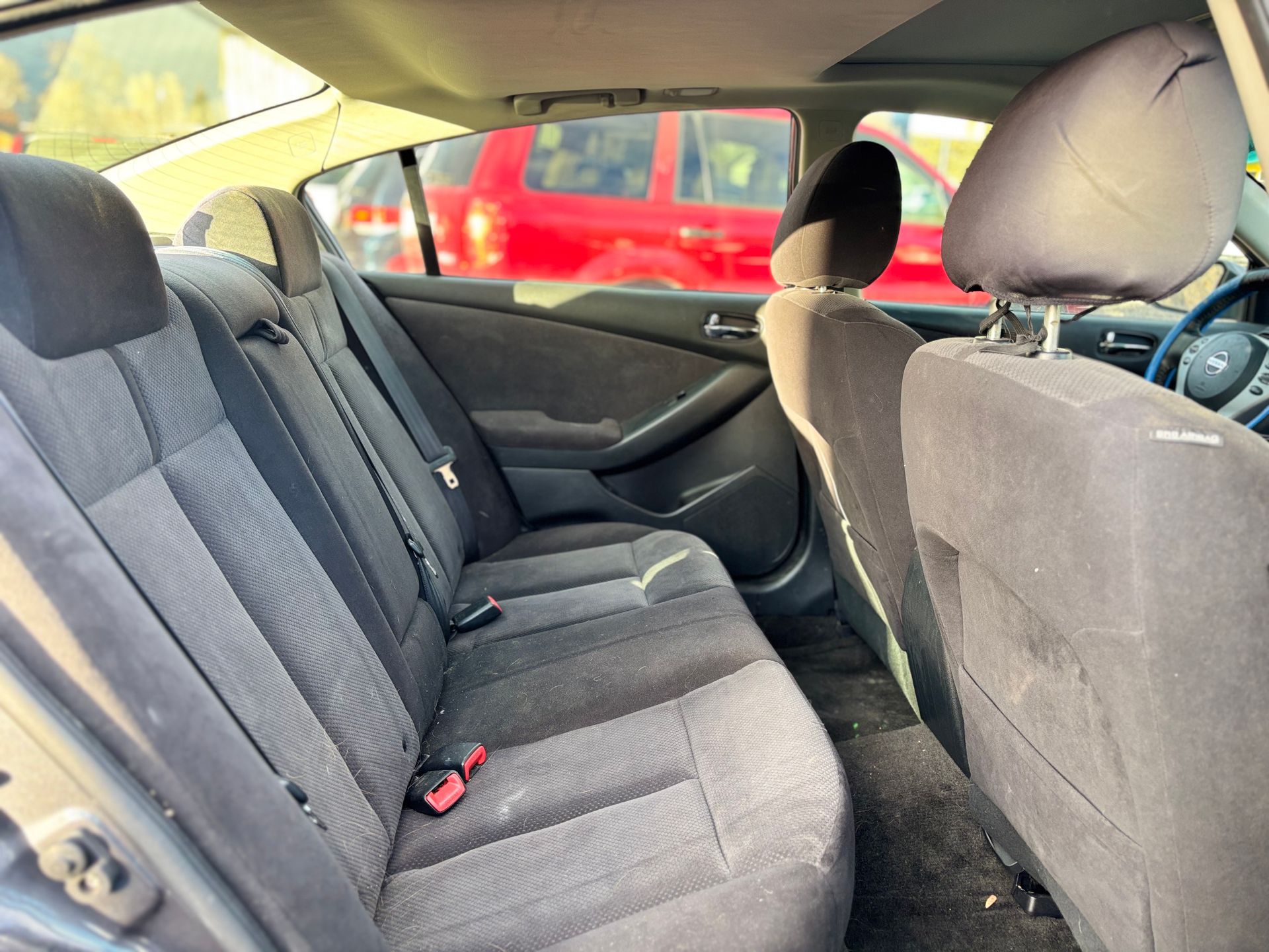 Black car interior, rear seats, black fabric. Red car visible through windows.