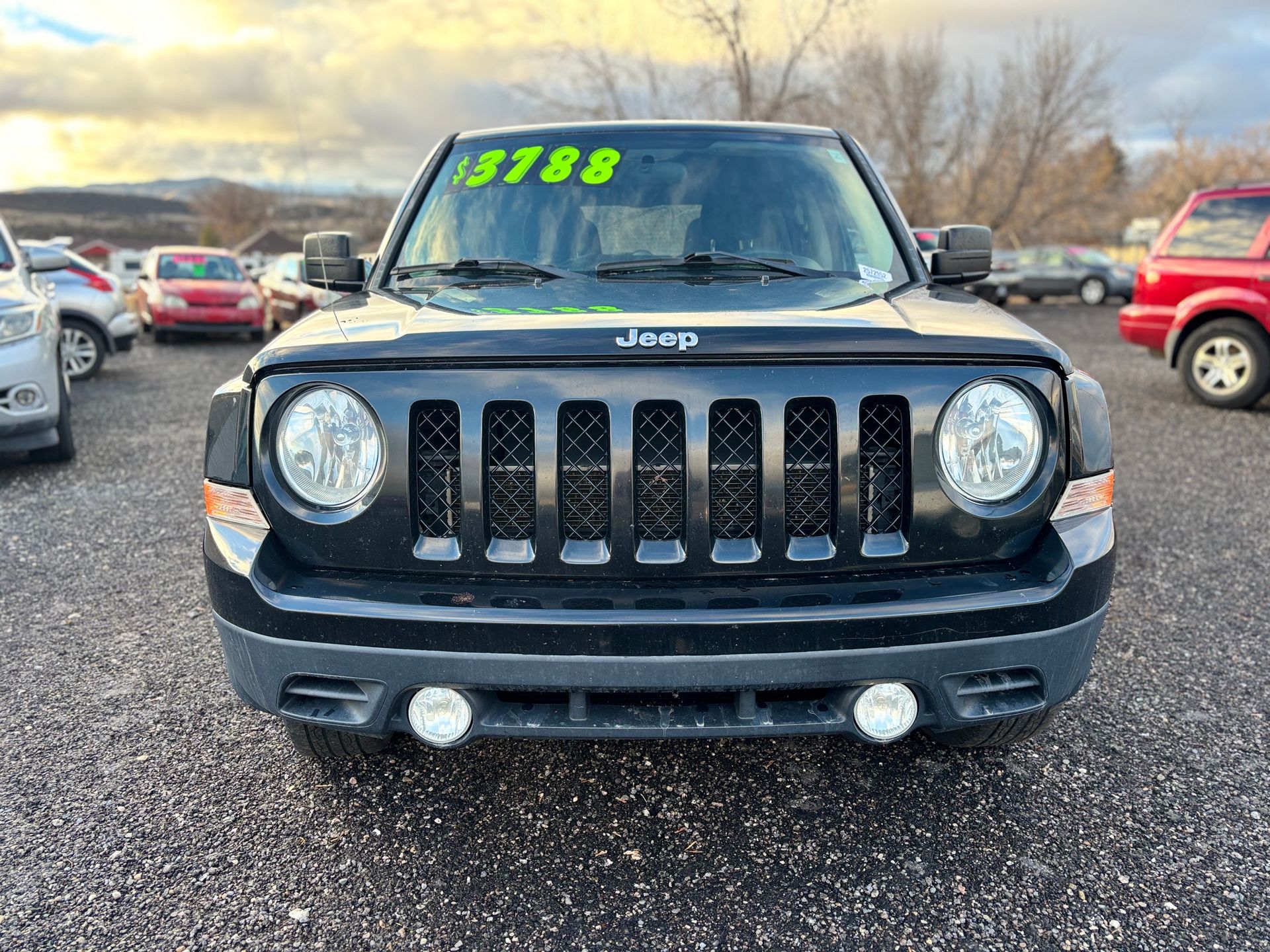 Black Jeep Patriot with round headlights and a black grill in a car lot.