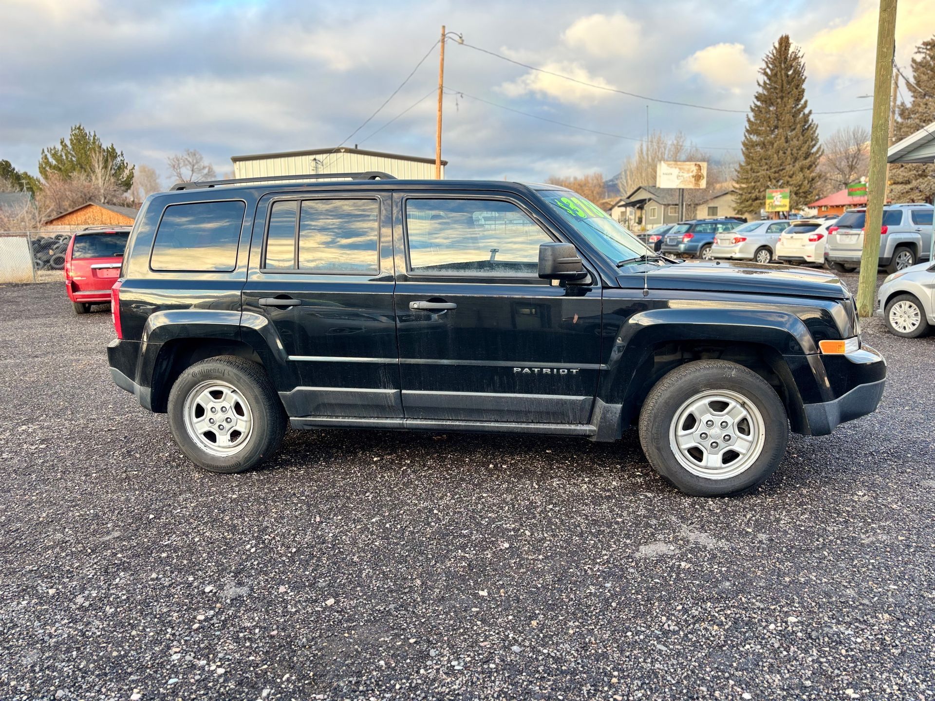 Black Jeep Patriot parked on gravel lot.