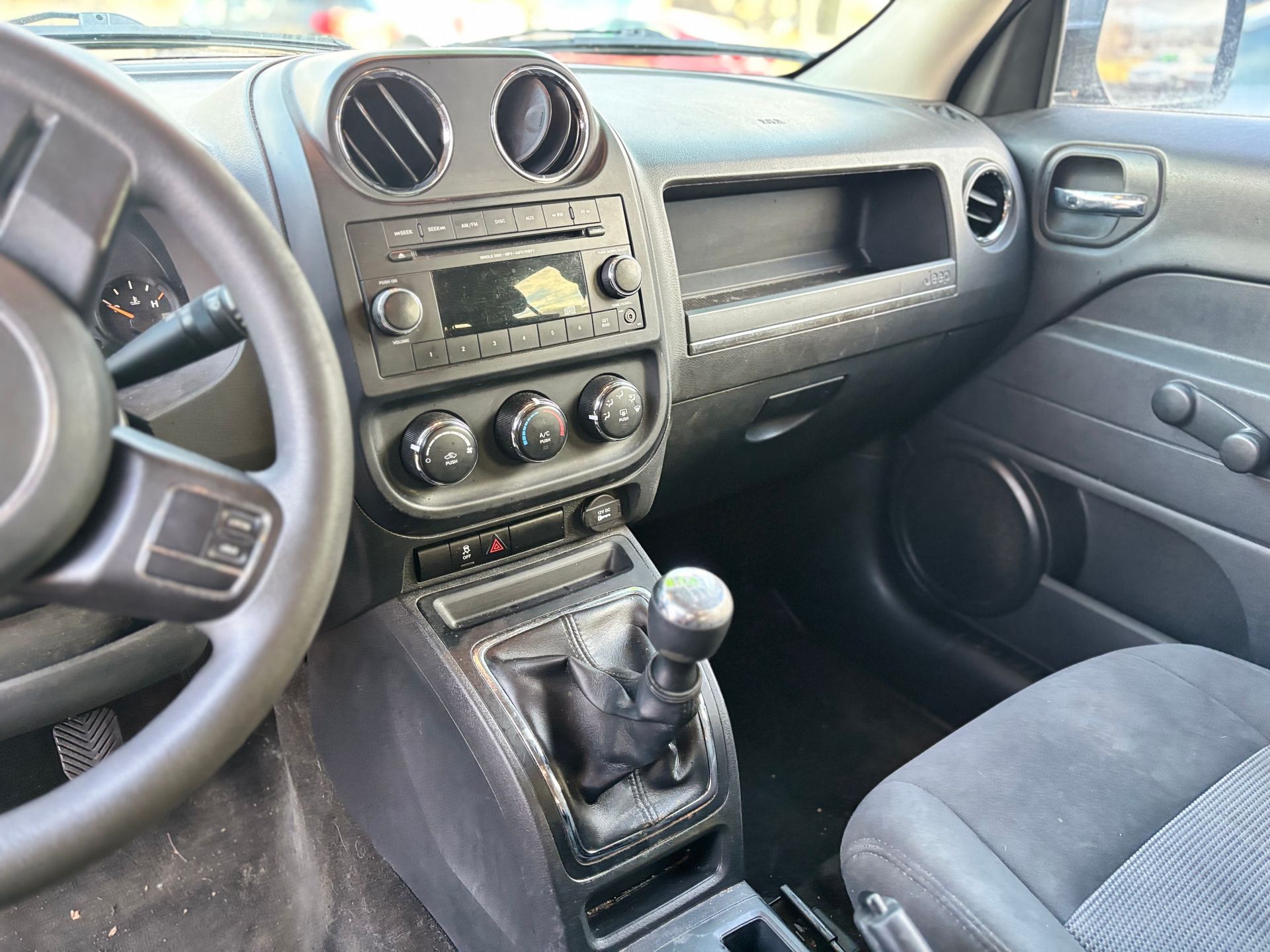 Interior view of a black Jeep Compass dashboard, including the steering wheel, stereo, and manual gear shift.