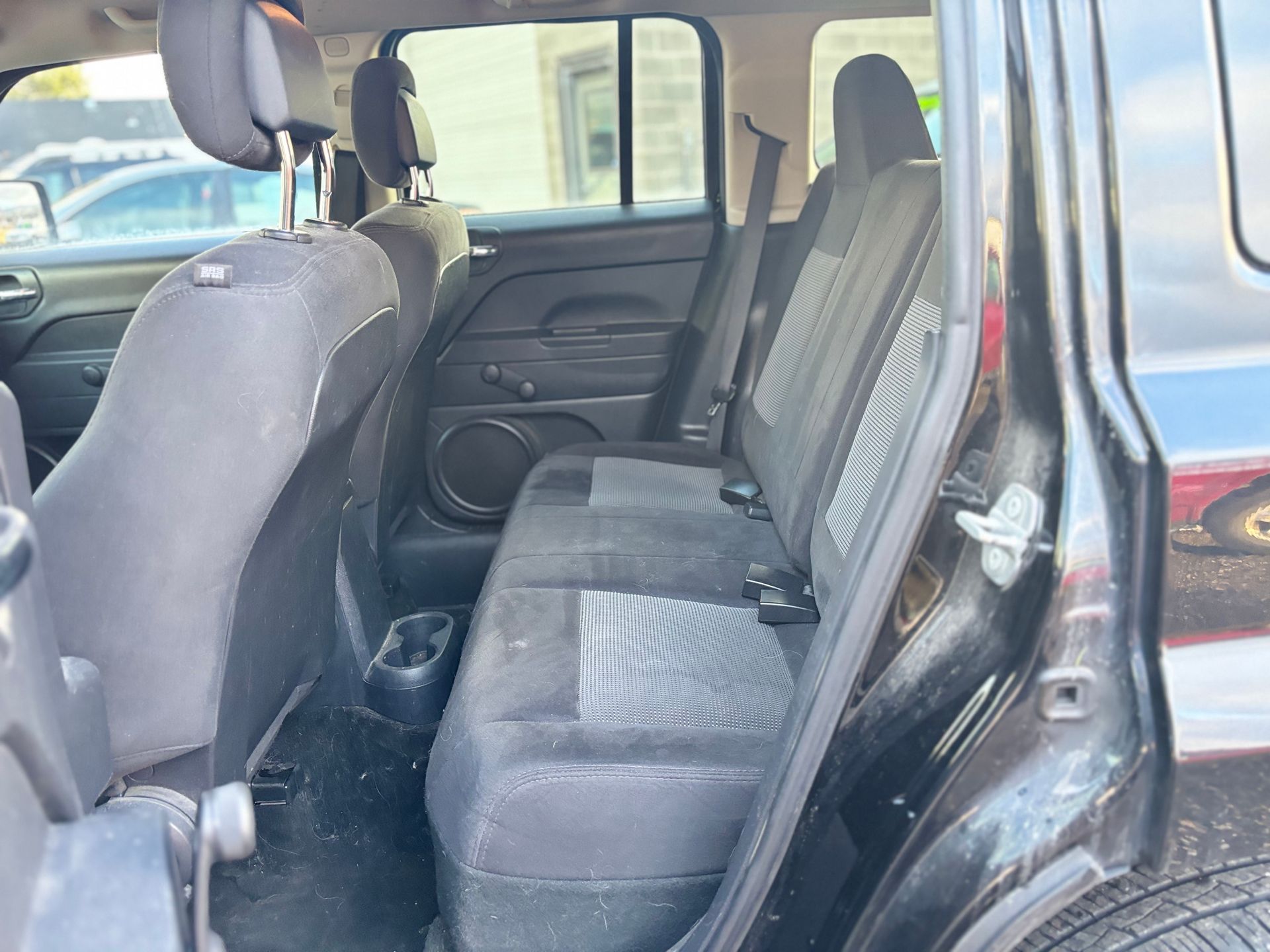 Interior view of a black SUV's back seat. The seats are gray, and there are two cup holders in the middle.