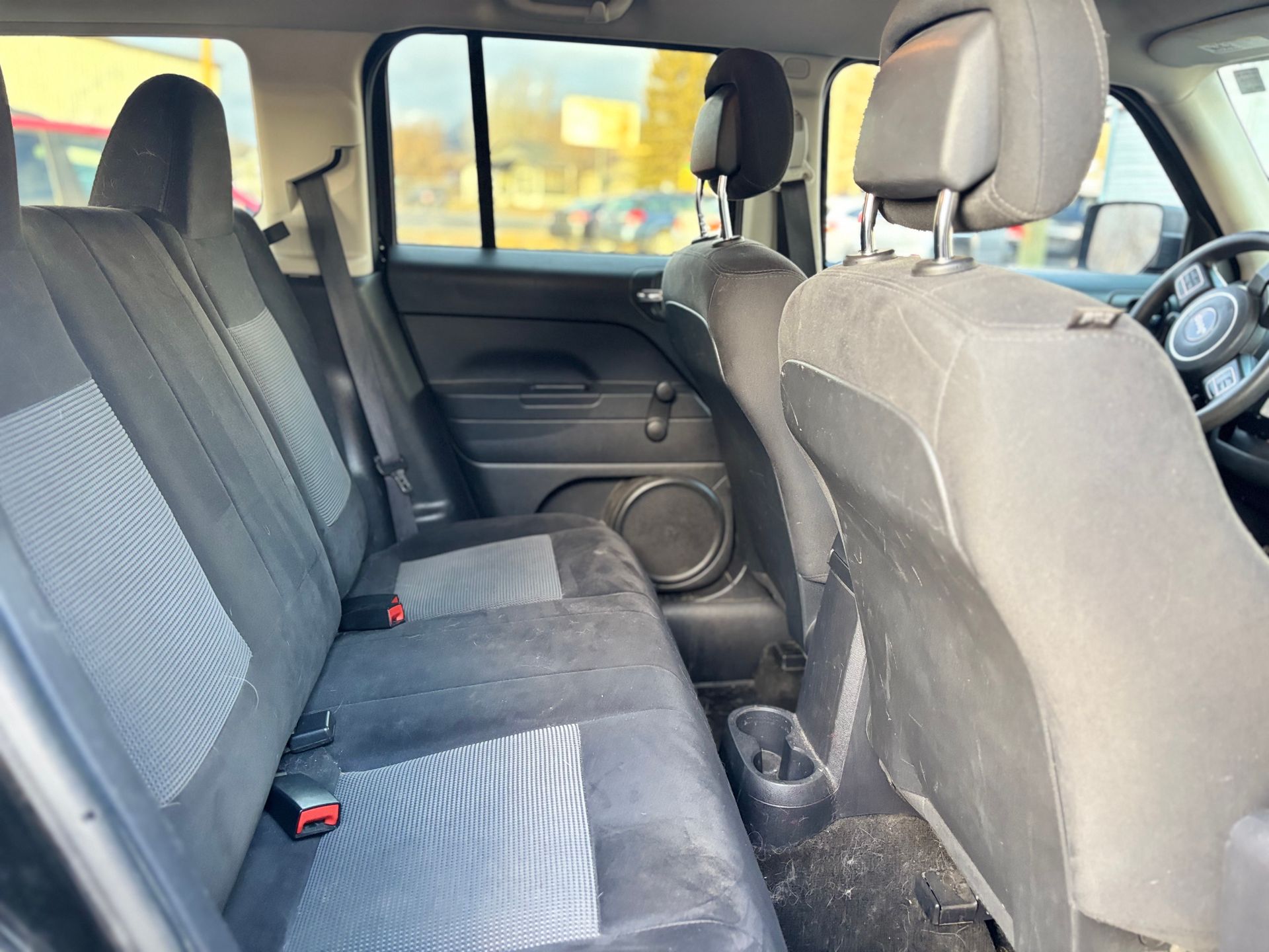 Interior of a black Jeep Patriot's backseats, showing fabric seats, headrests, and a cup holder.