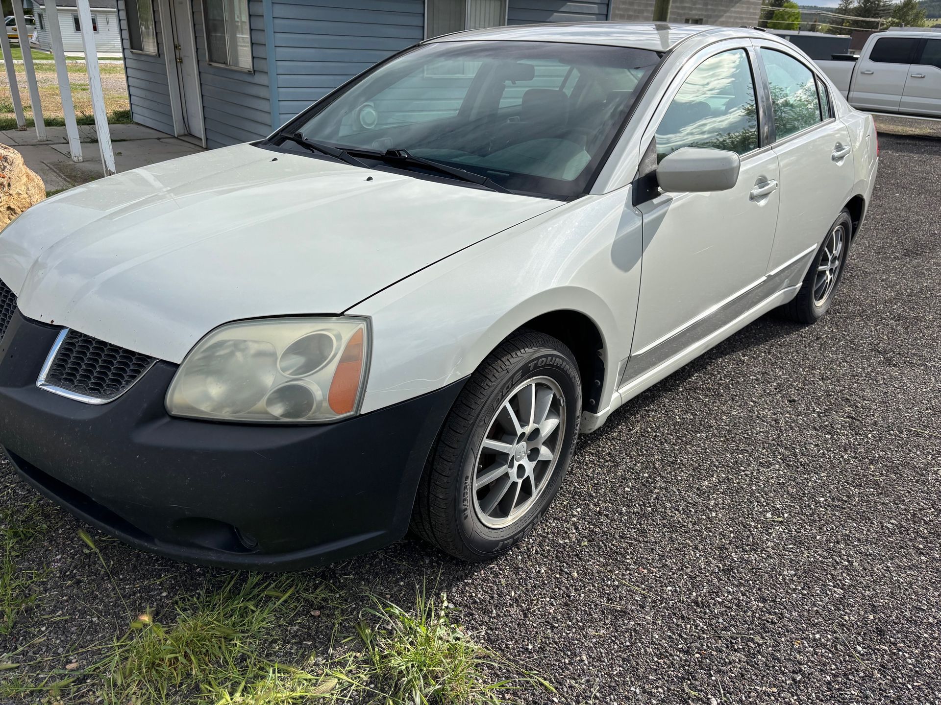 A white car is parked in a gravel lot.