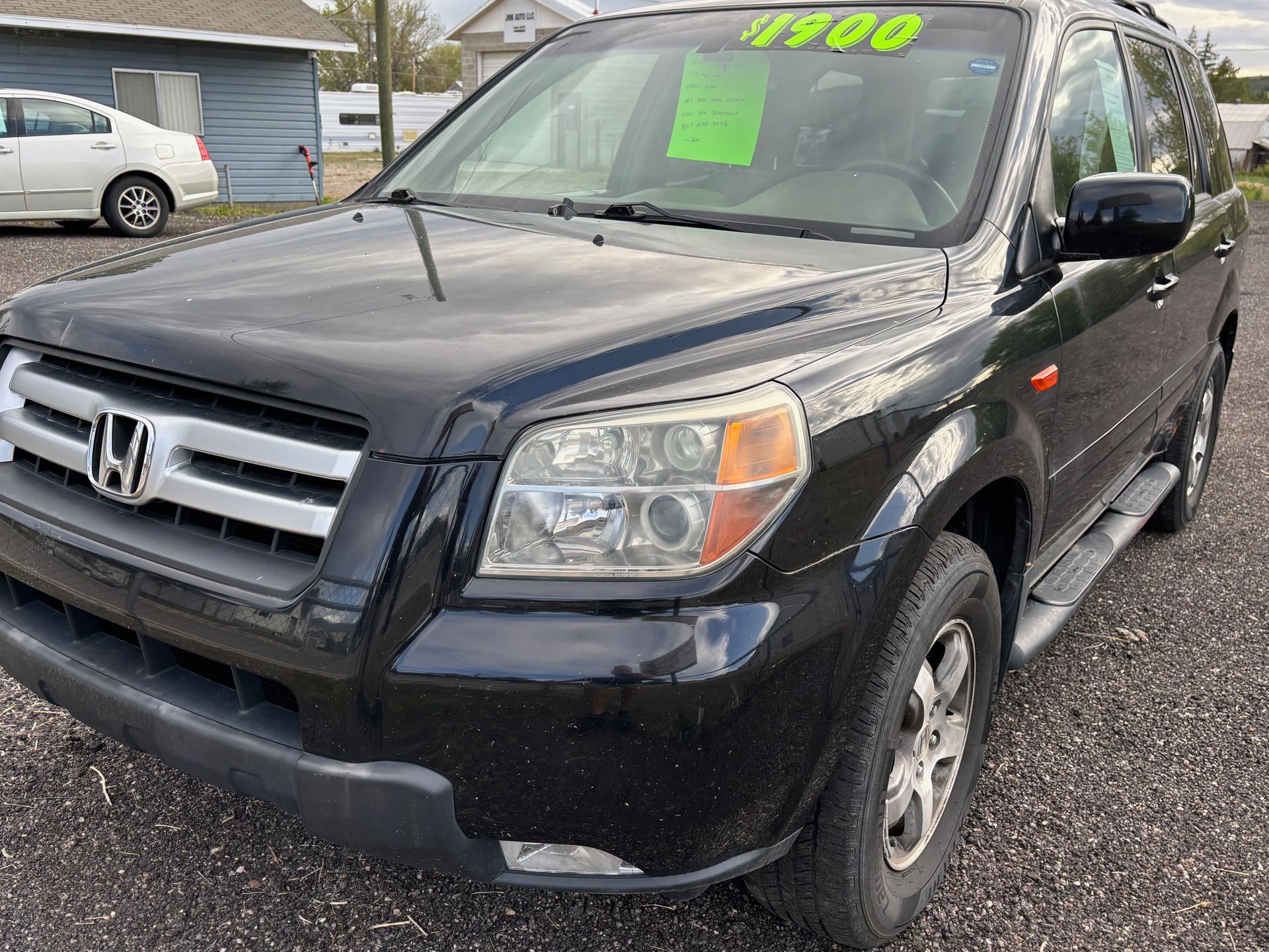 A black honda pilot is parked in a gravel lot.