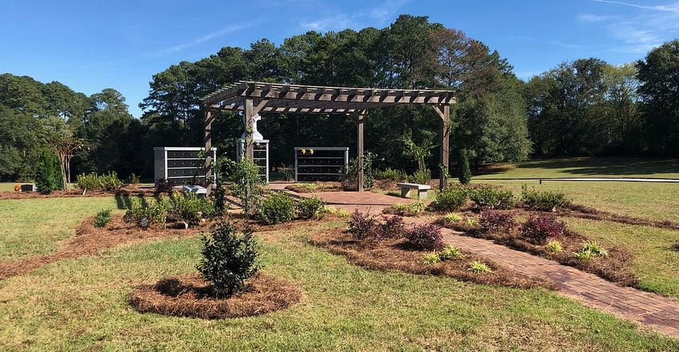 There is a pergola in the middle of a field with trees in the background.