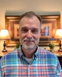 A man with a beard is wearing a plaid shirt and smiling for the camera.