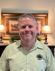 A man in a green shirt is smiling in front of a picture on the wall.