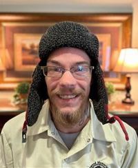 A man wearing a hat and glasses is smiling for the camera.