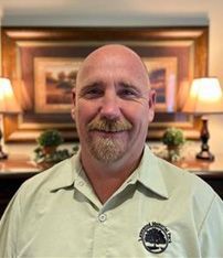 A bald man with a beard is wearing a black shirt and smiling.