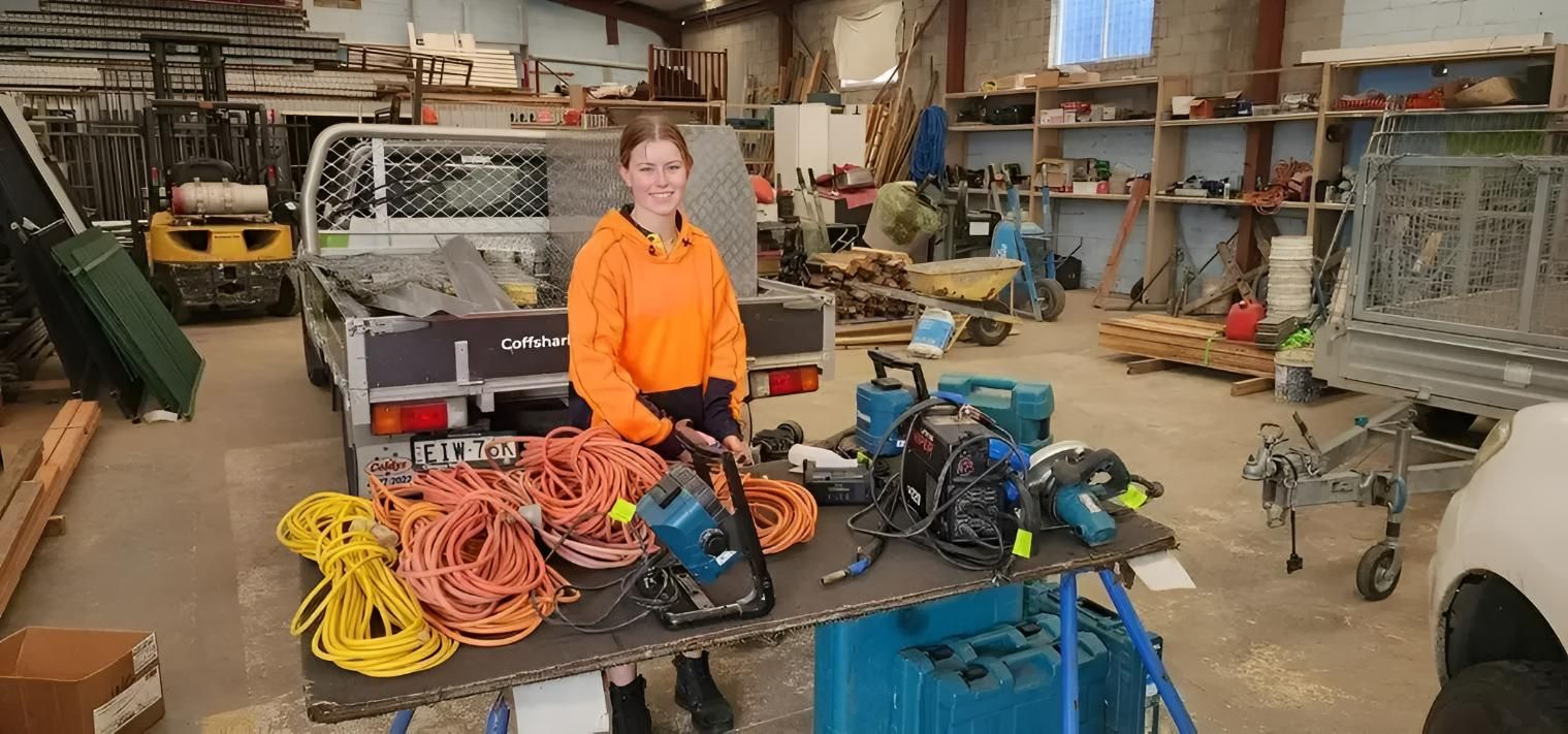 A Woman is Standing Next to a Table With Tools in a Garage — Coastal Test & Tag in Grafton, NSW