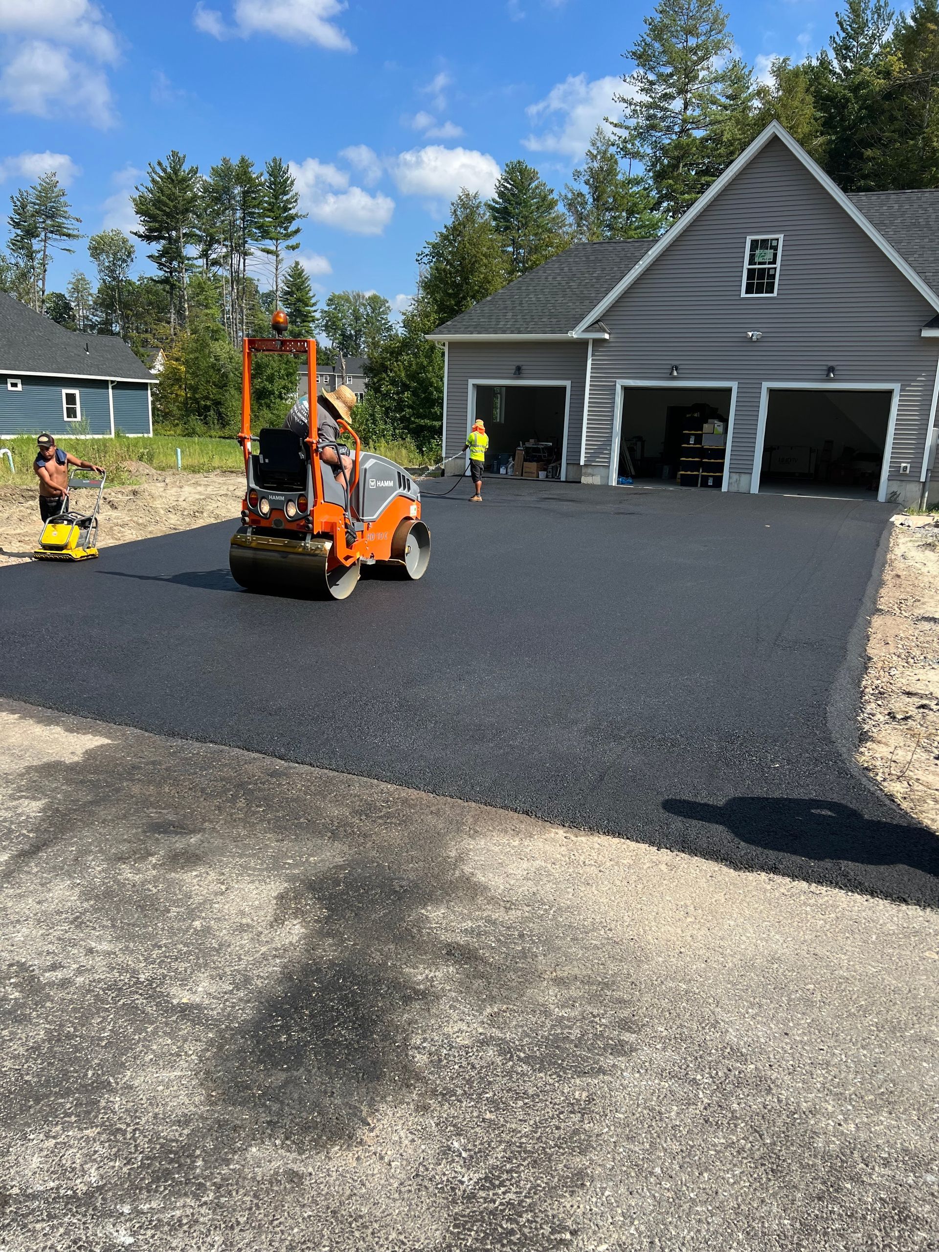 A roller is rolling asphalt in front of a house